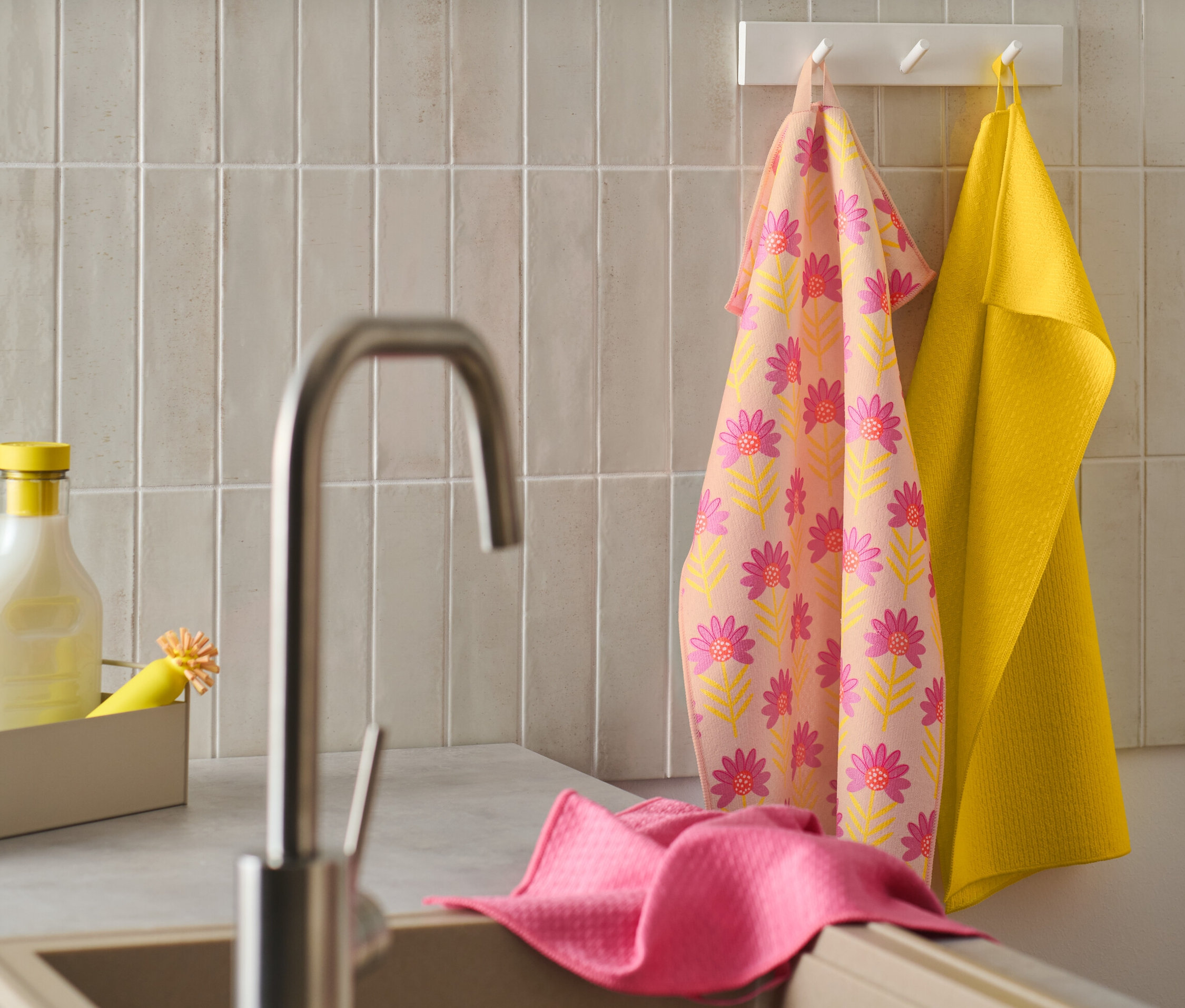 Ein blumengemustertes 3 Geschirrtücher und ein gelbes Geschirrtuch hängen an einem Haken. Ein rosa Geschirrtuch liegt auf dem Rand der Spüle.