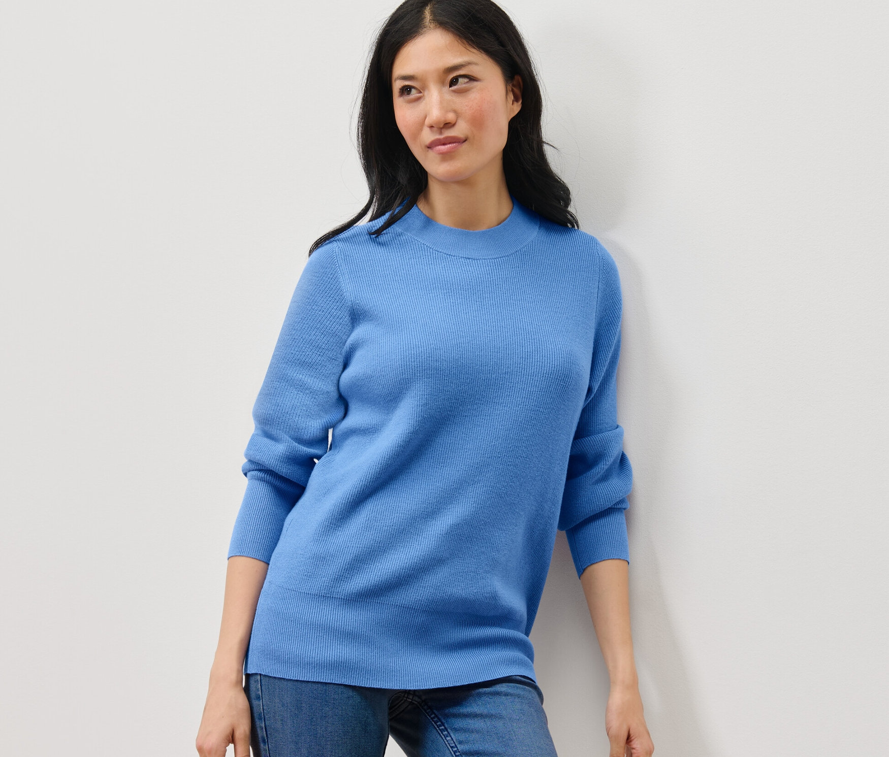 Frau posiert in blauem Feinstrickpullover und Jeans.