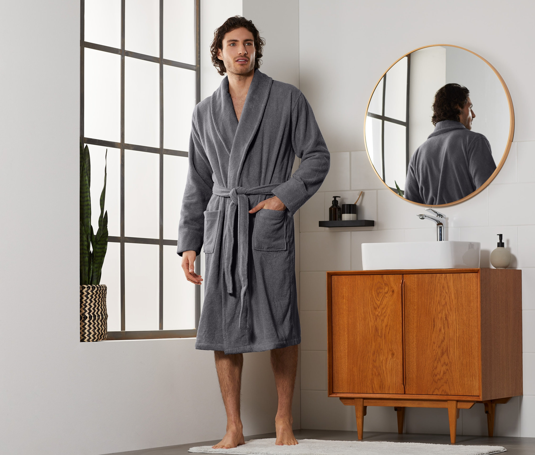 Ein Mann im grauen Herren-Bademantel steht im Badezimmer.