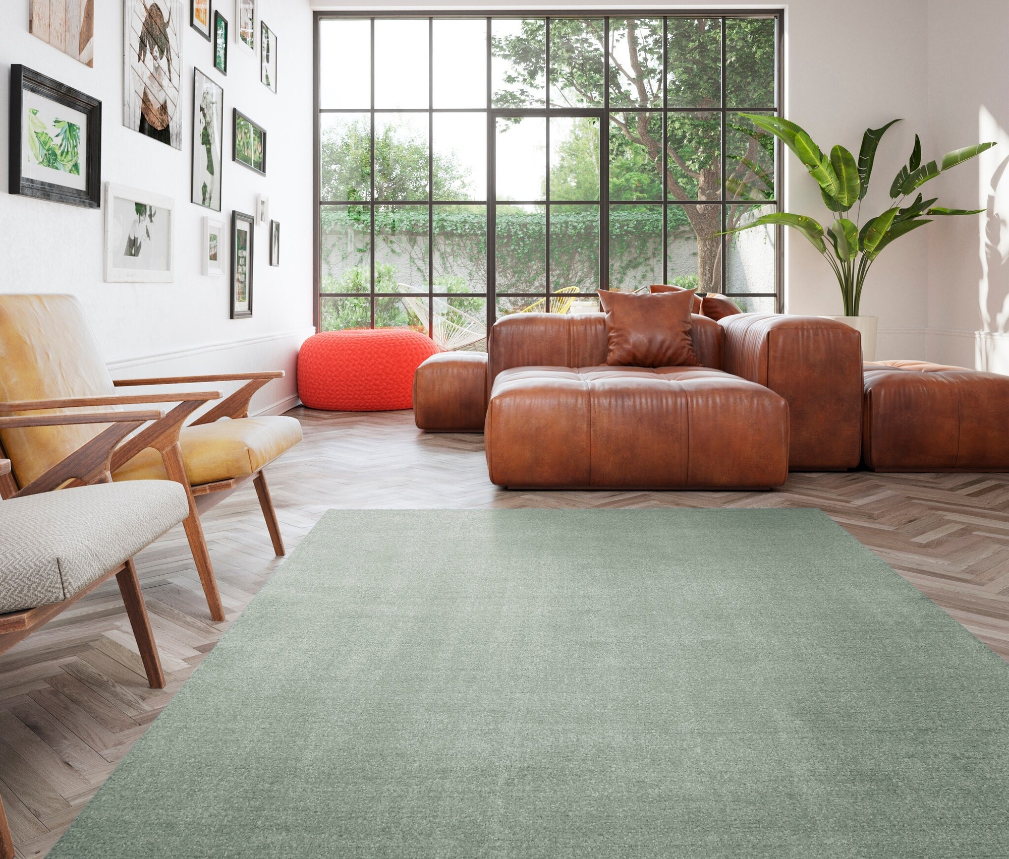 Wohnzimmer mit braunem Ledersofa, orangefarbenem Hocker und grünem Teppich »Mellow«.