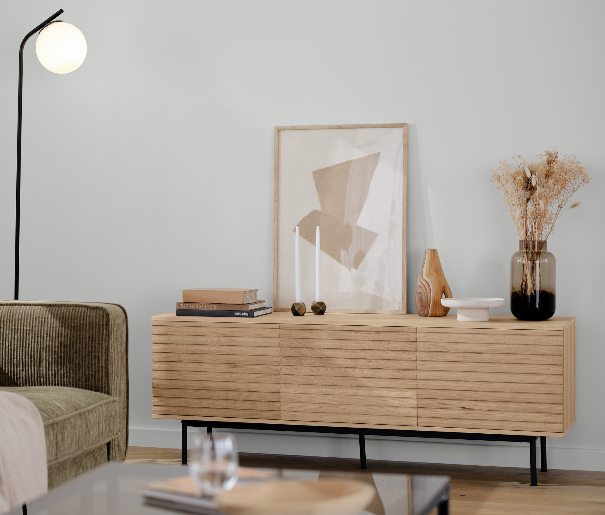 Ein braun-graues 3-Sitzer-Cordsofa, eine schwarze Stehleuchte mit Glaskugel, ein Lowboard »Finnsbo« und ein zweiteiliges Couchtisch-Set in einem Wohnzimmer.