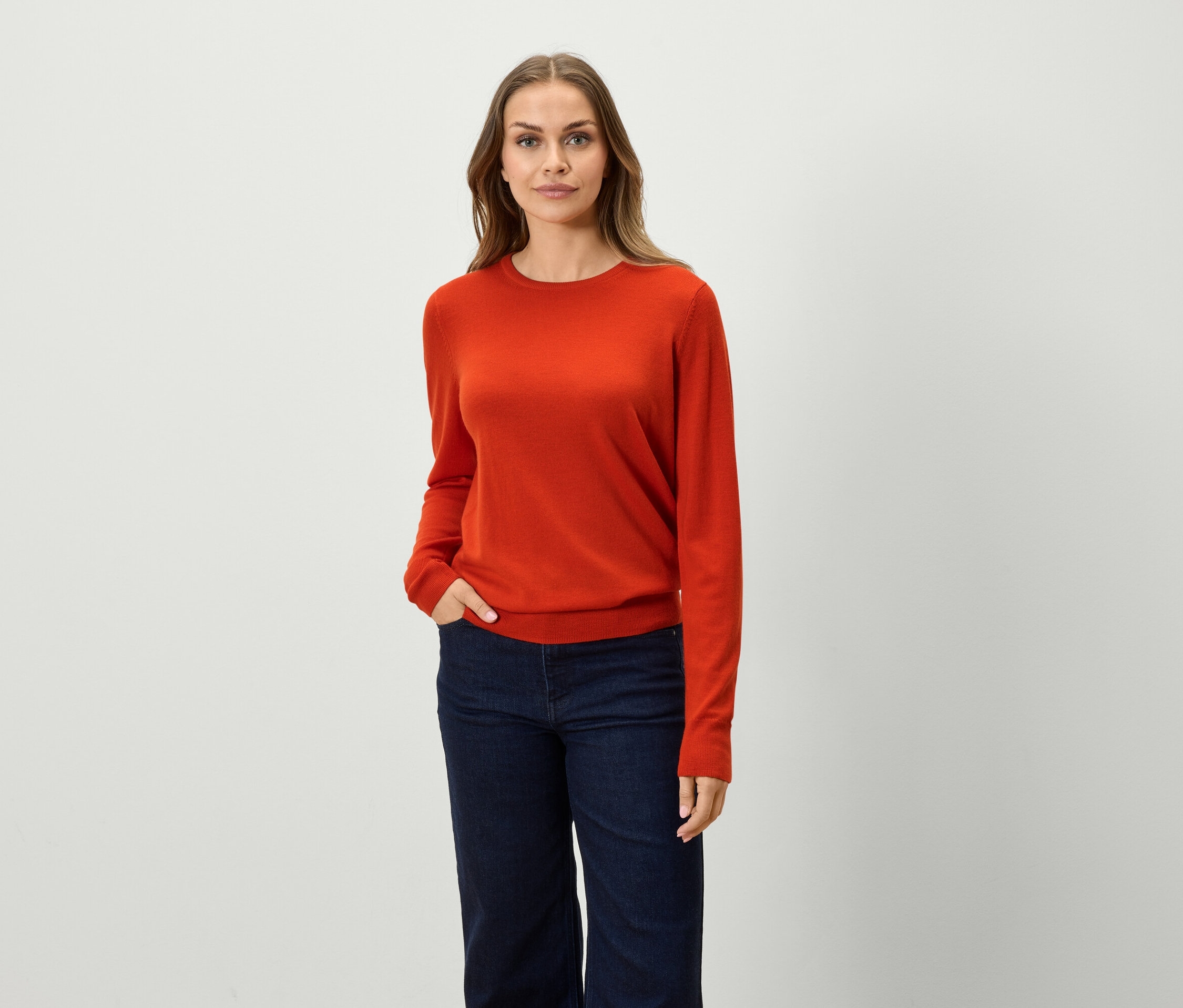 Frau posiert in orangefarbenem Pullover und blauen Jeans.