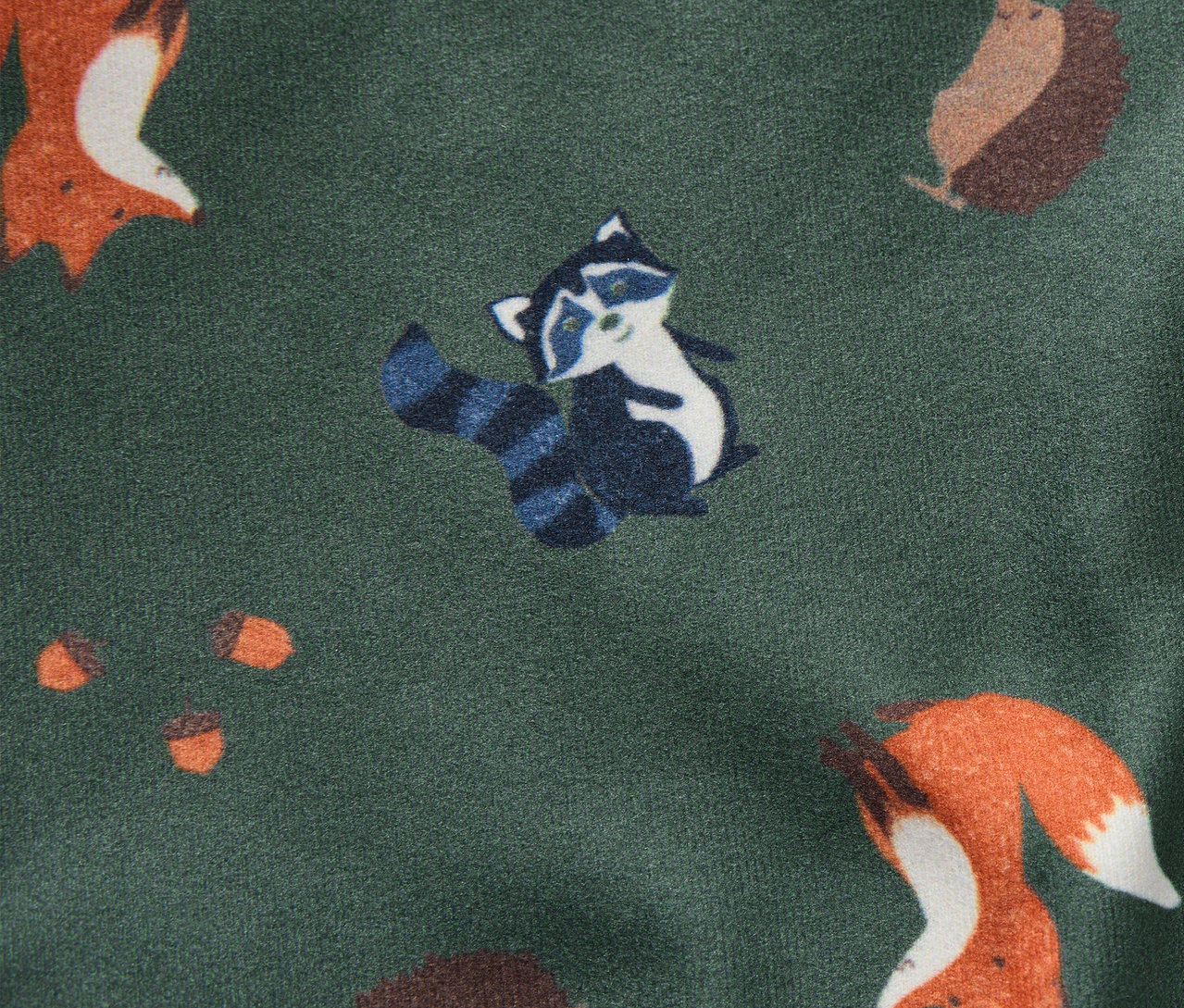 Muster einer Kinder-Wende-Schlupfmütze mit Füchsen, Waschbären, Igeln und Eicheln auf grünem Hintergrund.