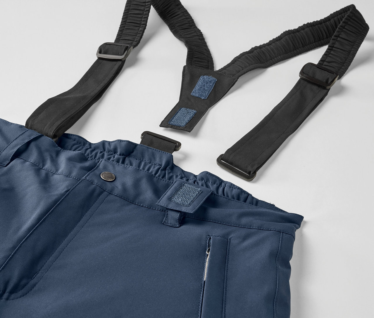 Detail einer blauen Hose mit schwarzen, elastischen Hosenträgern.