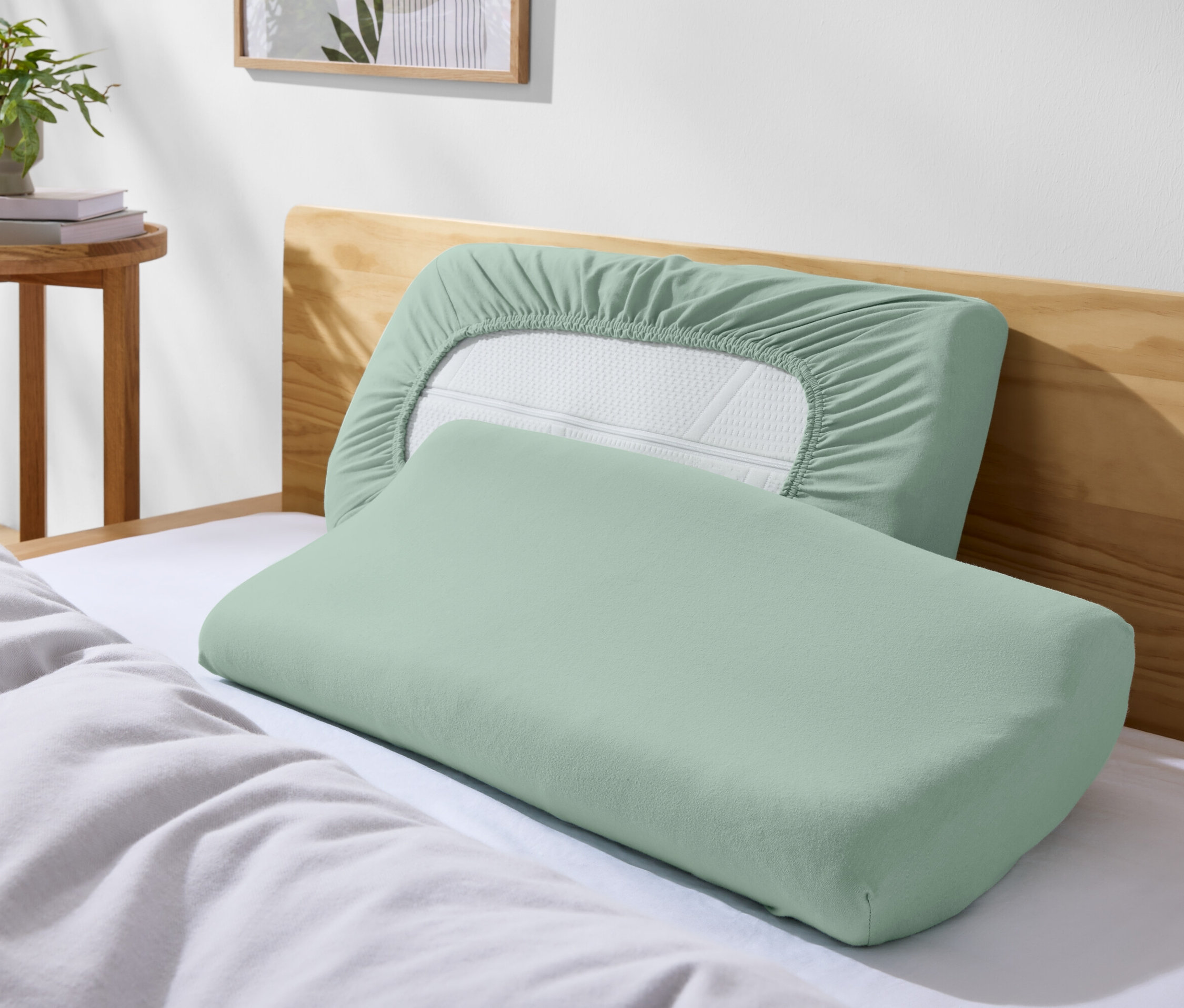 Zwei grüne Kissen auf einem Bett mit weißer Bettwäsche.