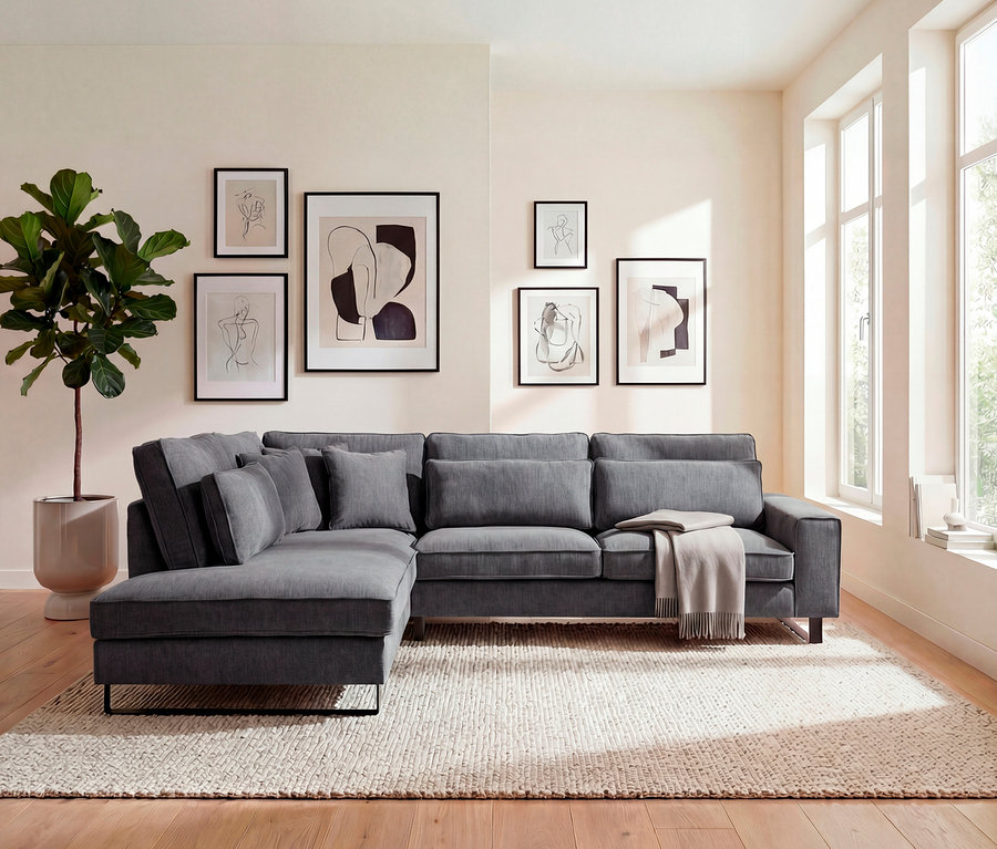 Wohnzimmer mit grauem Ecksofa, Kissen, Decke, Zimmerpflanze und sechs gerahmten Kunstdrucken an der Wand über einem beige Teppich.