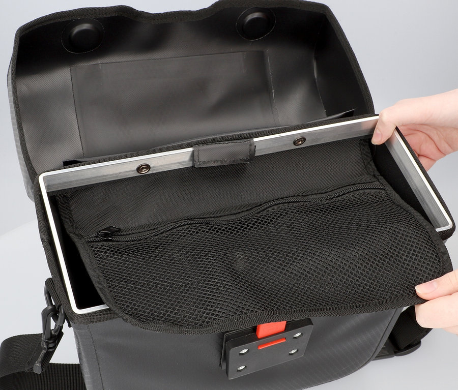 Hände öffnen eine schwarze FISCHER Lenkertasche PLUS+ Terra, die eine Netztasche und eine silberne Halterung zeigt.