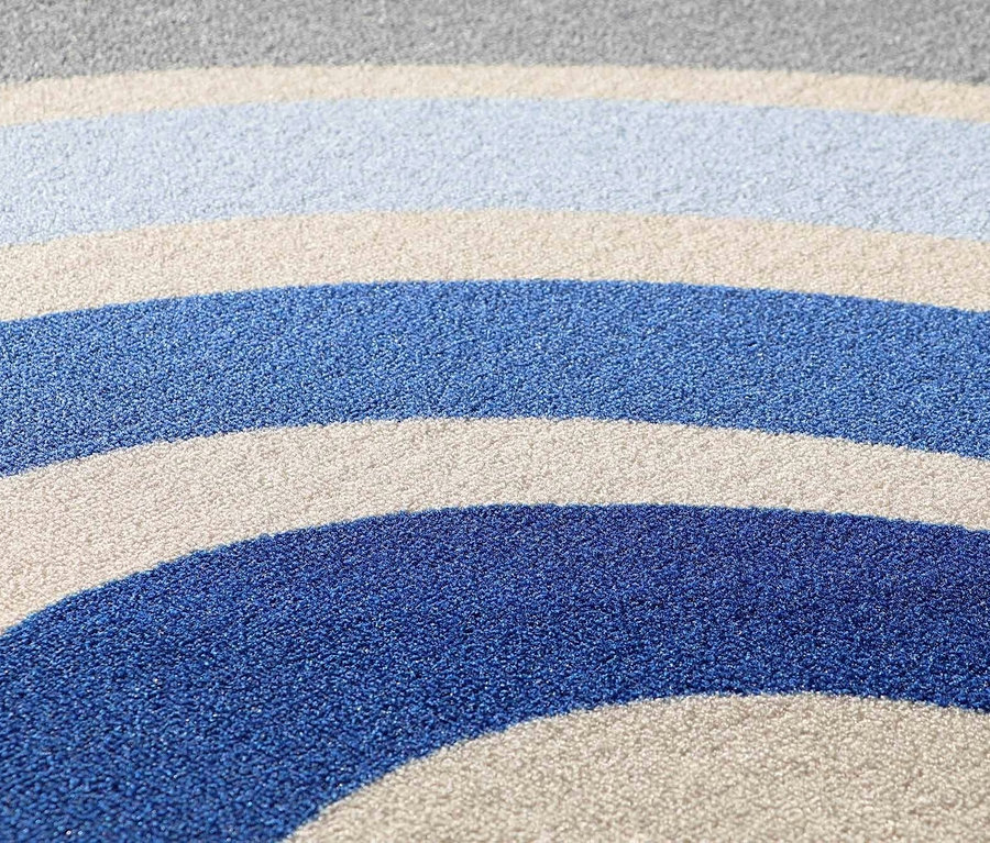 Nahaufnahme eines blauen Kinderteppichs »Rainbow« mit Streifen in verschiedenen Blautönen, Beige und Grau.