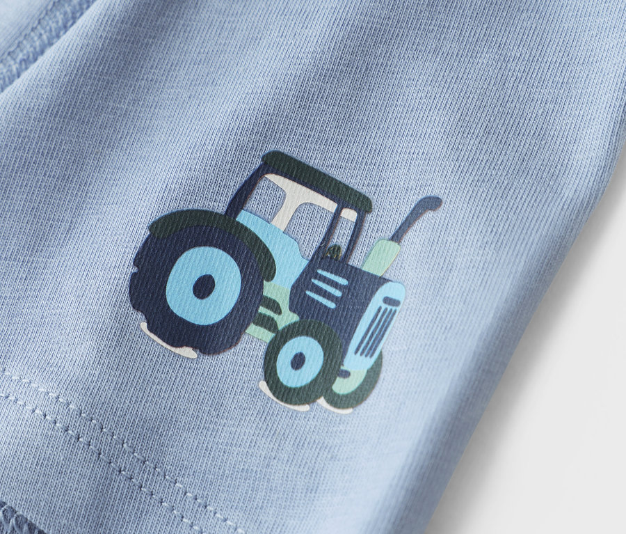 Detailaufnahme eines hellblauen Stoffes mit einem Traktoraufdruck.