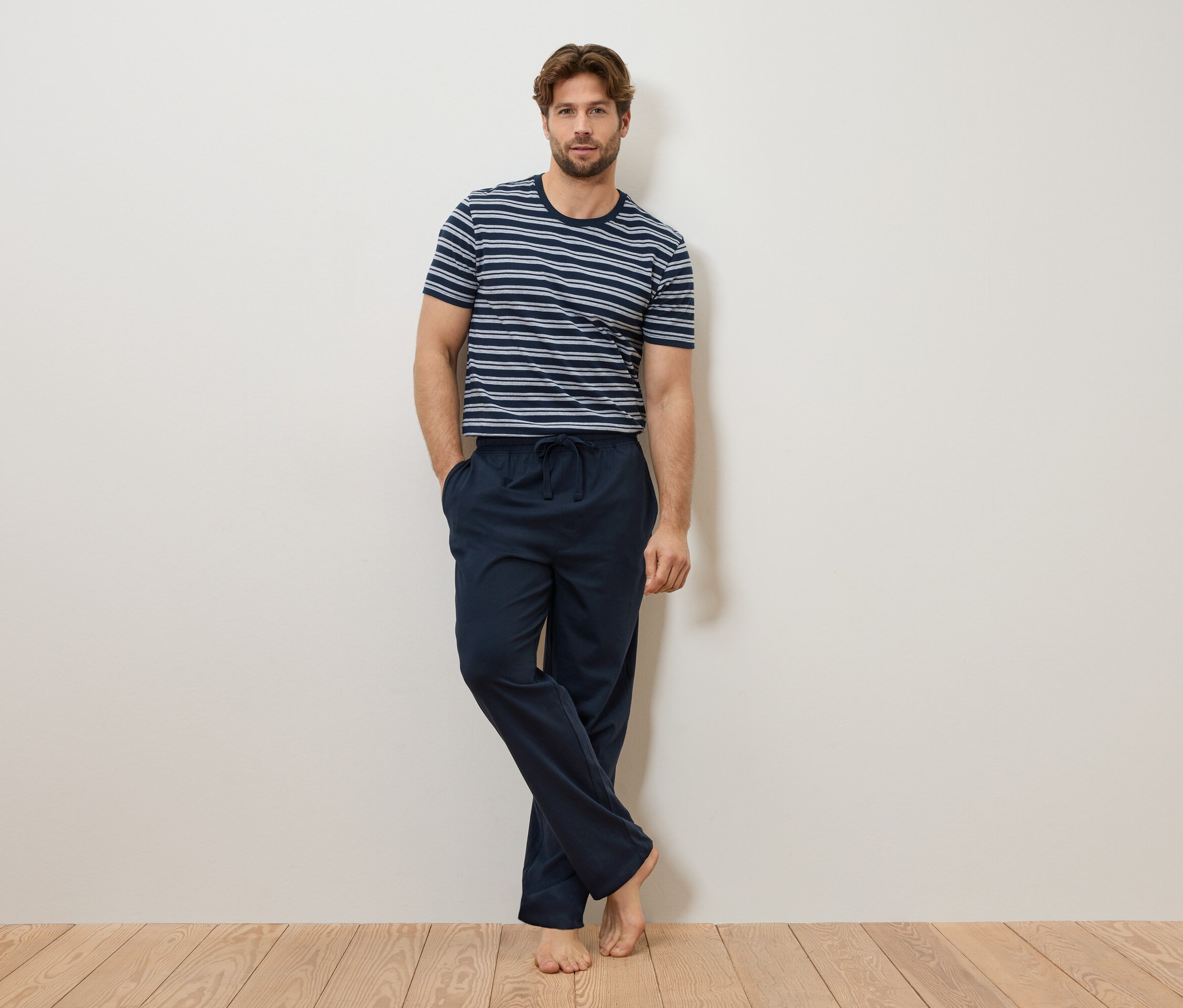 Mann lehnt an einer Wand, trägt ein blau-weiß gestreiftes T-Shirt und eine marineblaue Pyjamahose.