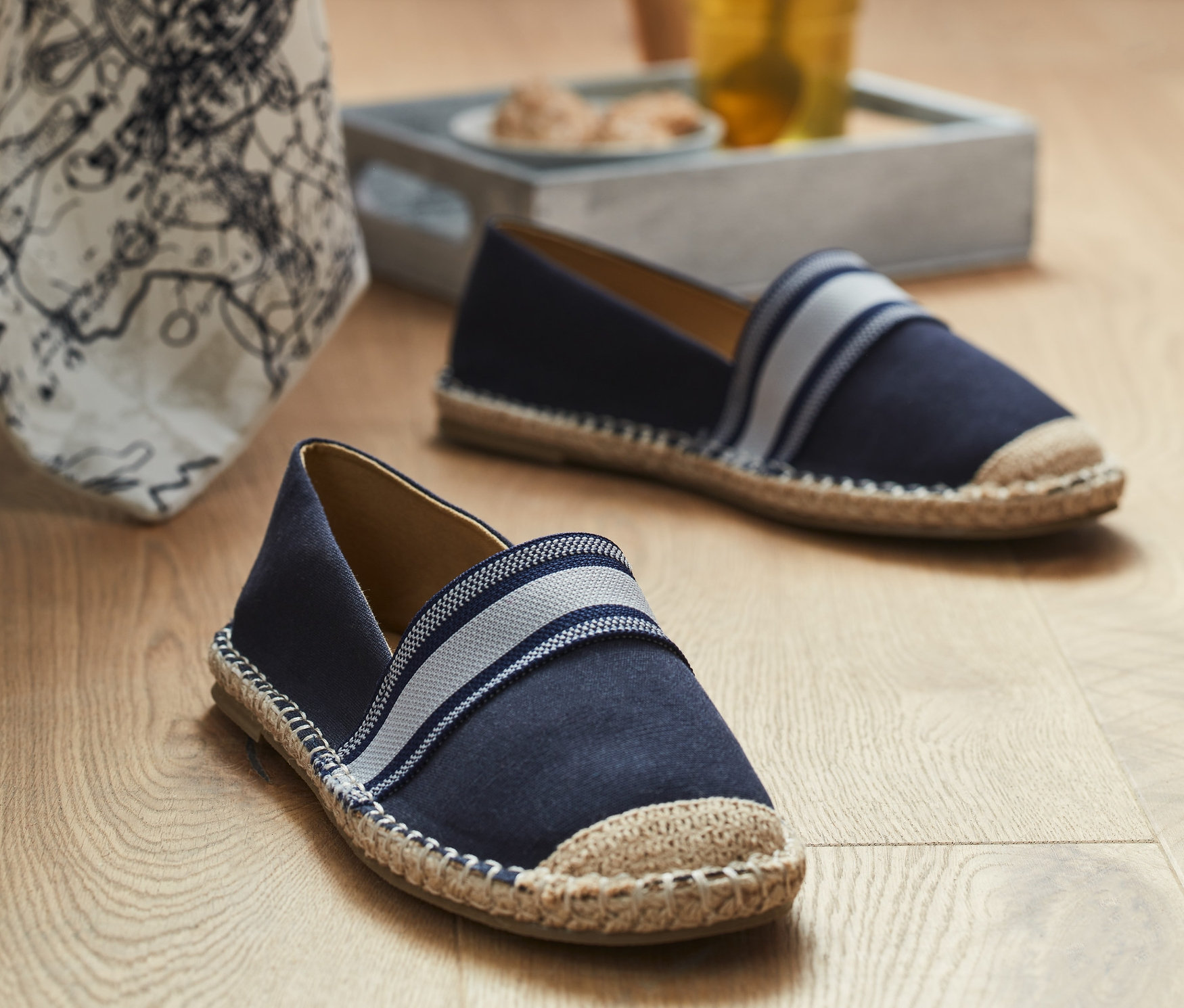 Zwei Espadrilles auf einem Holzboden in der Nähe eines Glases mit Getränk.