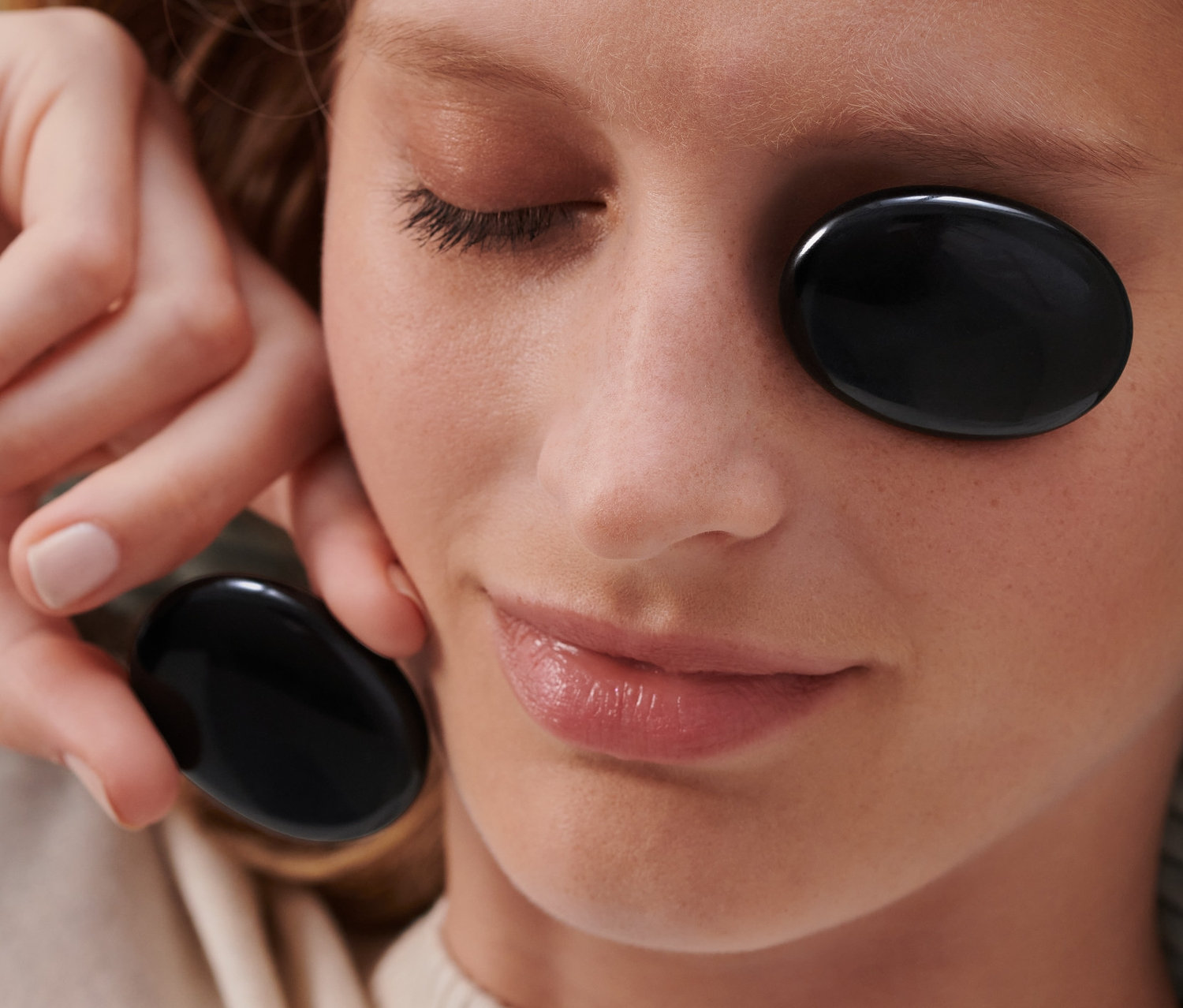Frau liegt mit Obsidian-Augen- und Meditationssteinen auf einem Auge und hält einen weiteren in der Hand.