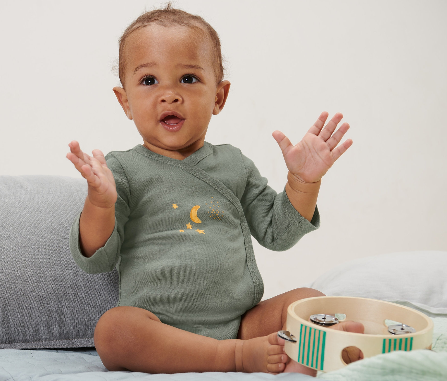 Sitzendes Baby winkt mit den Händen und trägt 5 Baby-Bodys mit Mitwachsfunktion, Sterne.