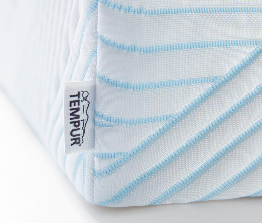 Detail einer Ecke des weißen TEMPUR Pro® Plus SmartCool™ Toppers mit blauen Streifen und Markenetikett.