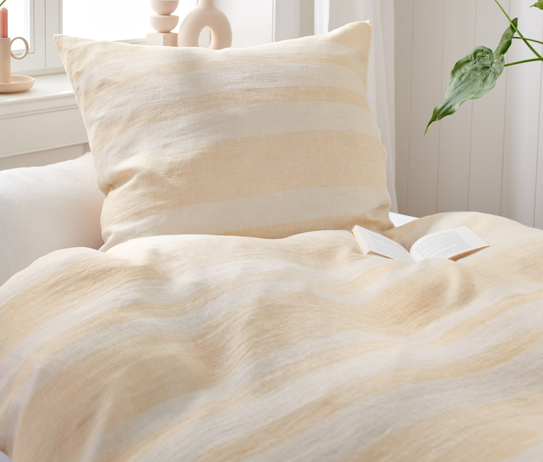 Nahaufnahme eines Bettes mit Bettwäsche aus gewaschenem Leinen und einem offenen Buch.