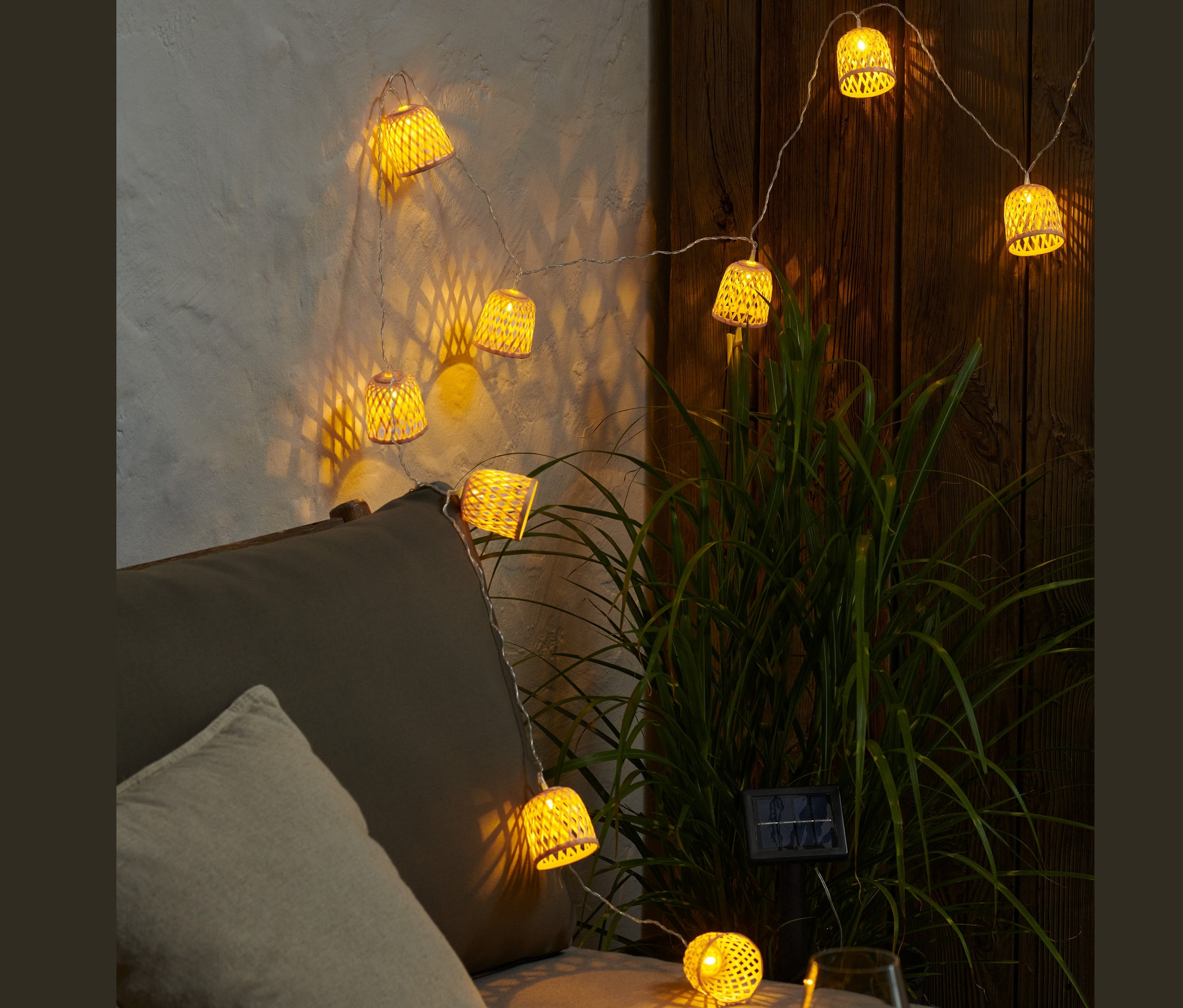 Eine leuchtende Solar-Lichterkette mit dekorativen Schirmen hängt über einem grauen Sofa.