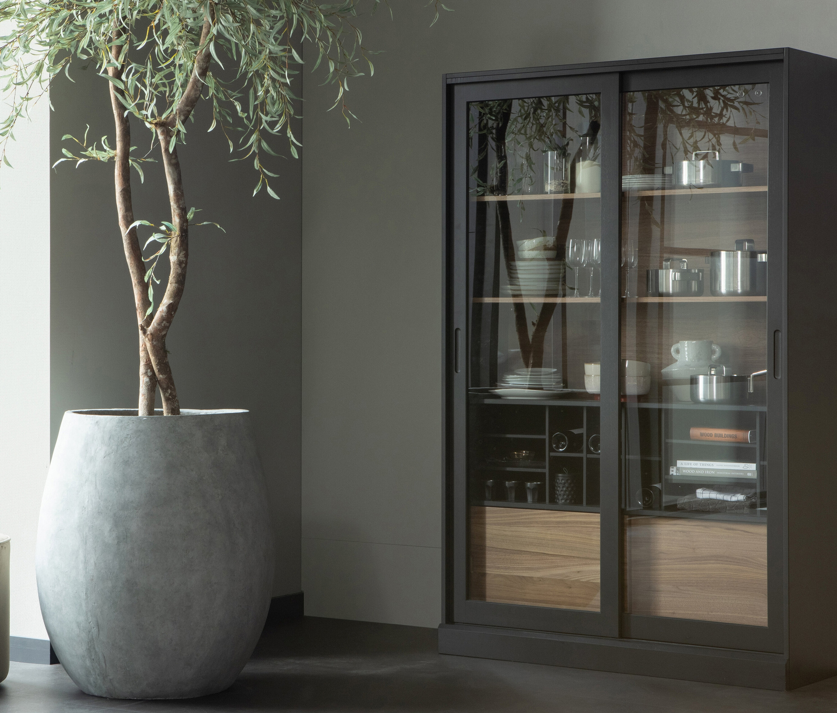Innenraum mit großem Topf und schwarzer Glasvitrine. Zu sehen ist die Woood Vitrine »James« aus Kiefernholz, schwarz.
