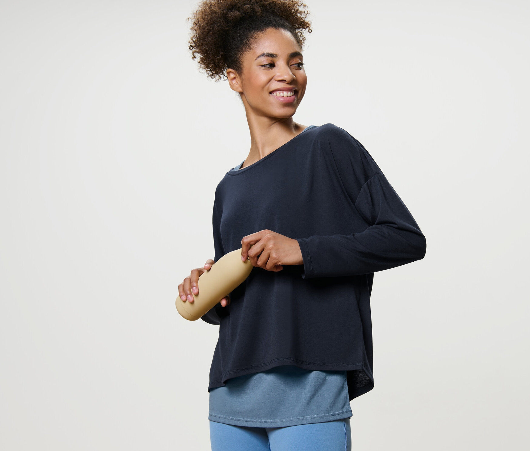 Frau hält Wasserflasche und trägt blaues 2-in-1-Sportshirt.