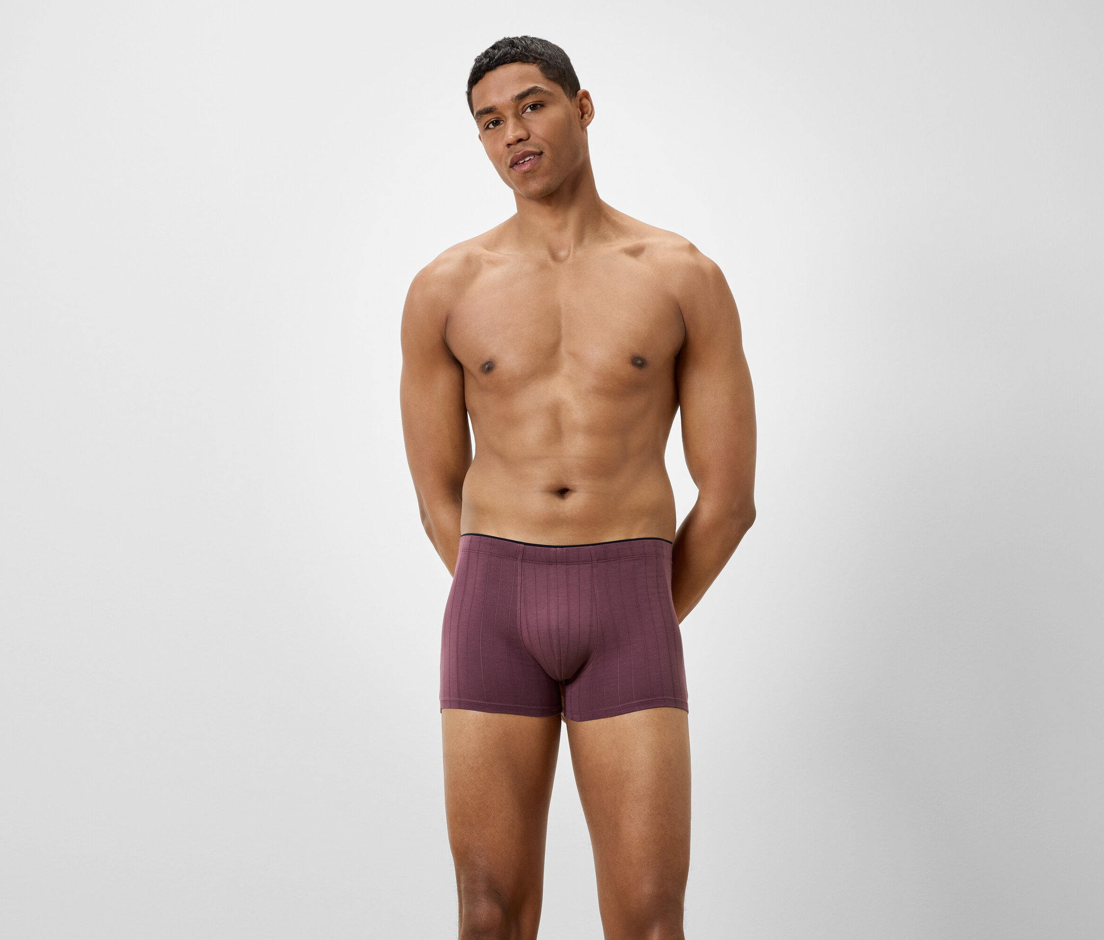 Mann posiert vor hellem Hintergrund in burgunderfarbenen Boxershorts.