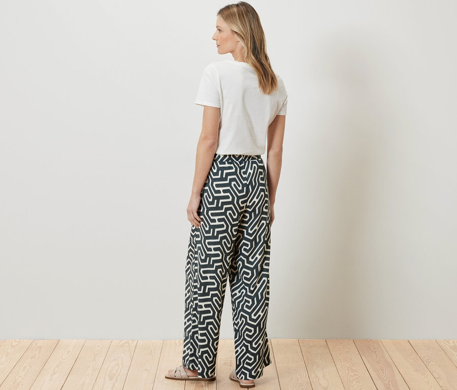 Eine Frau steht mit dem Rücken zur Kamera und trägt ein weißes T-Shirt und eine bedruckte Schlupfhose in Crinkle-Optik.