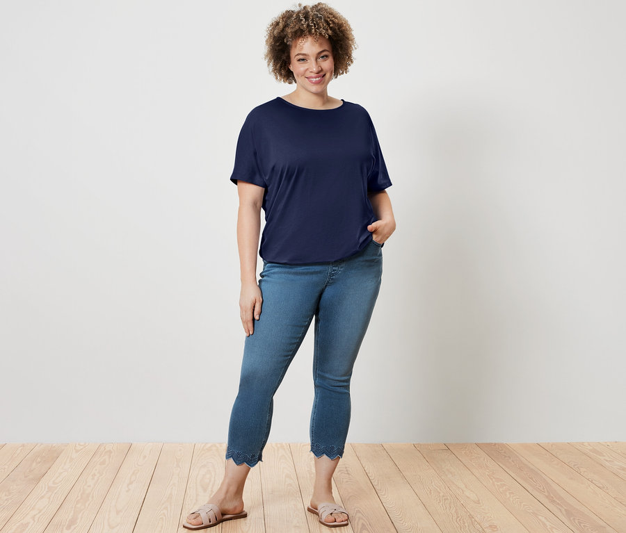 Frau posiert in dunkelblauem Blusenshirt und 7/8-Treggings mit Lochstickerei.