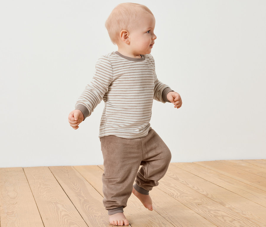 Ein Baby geht auf einem Holzboden und trägt ein Baby-Nicki-Set.