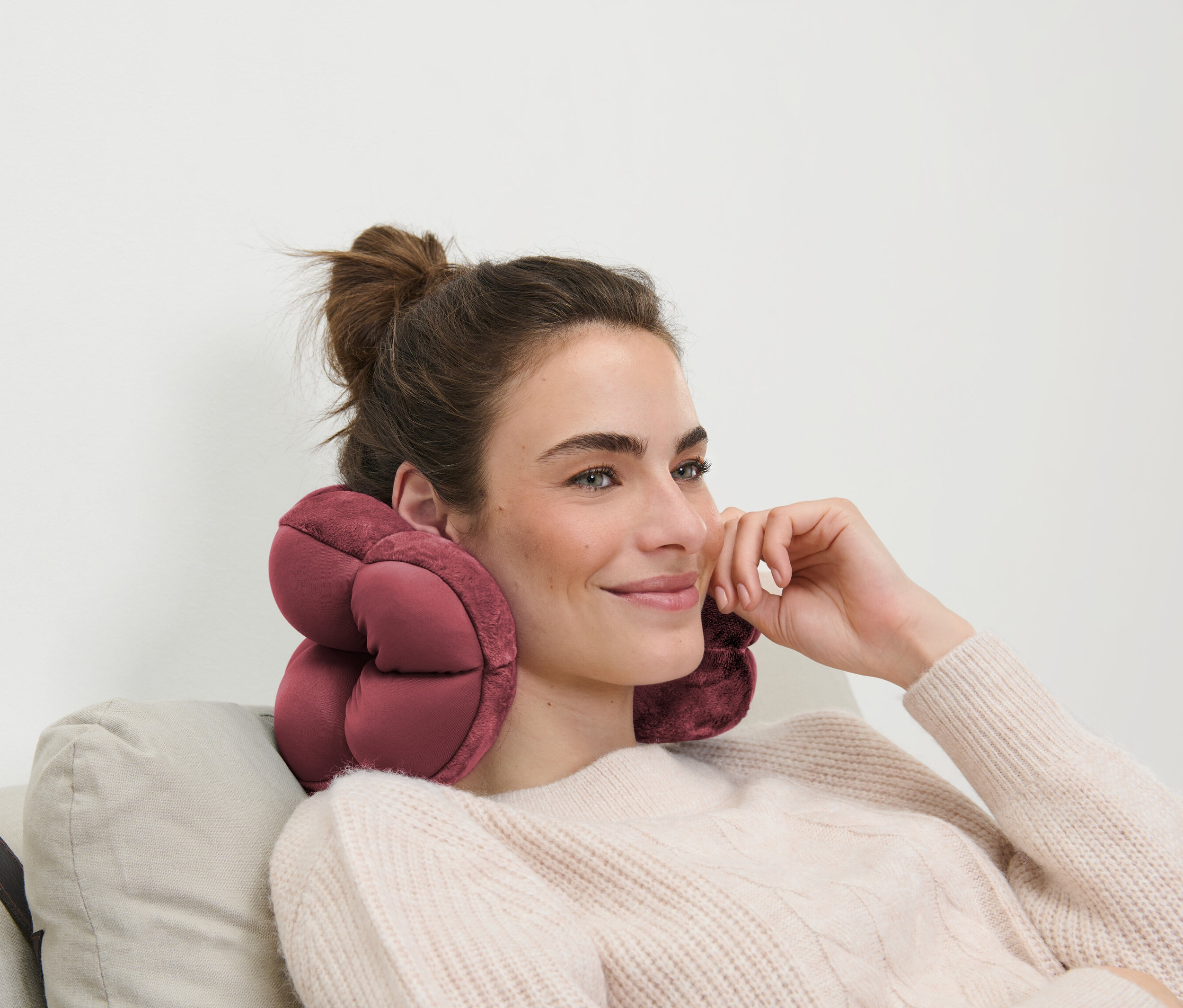 Frau mit braunen Haaren sitzt auf einem Sofa mit einem rosa Reisekissen um den Hals.
