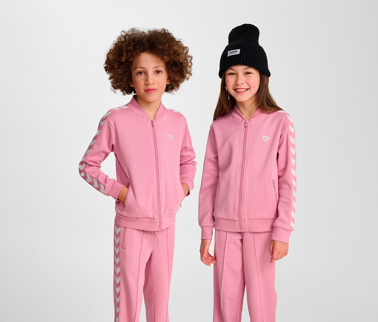 Zwei Kinder posieren in rosa Hummel HMLJR Archive Reg Poly Zip Jacken.