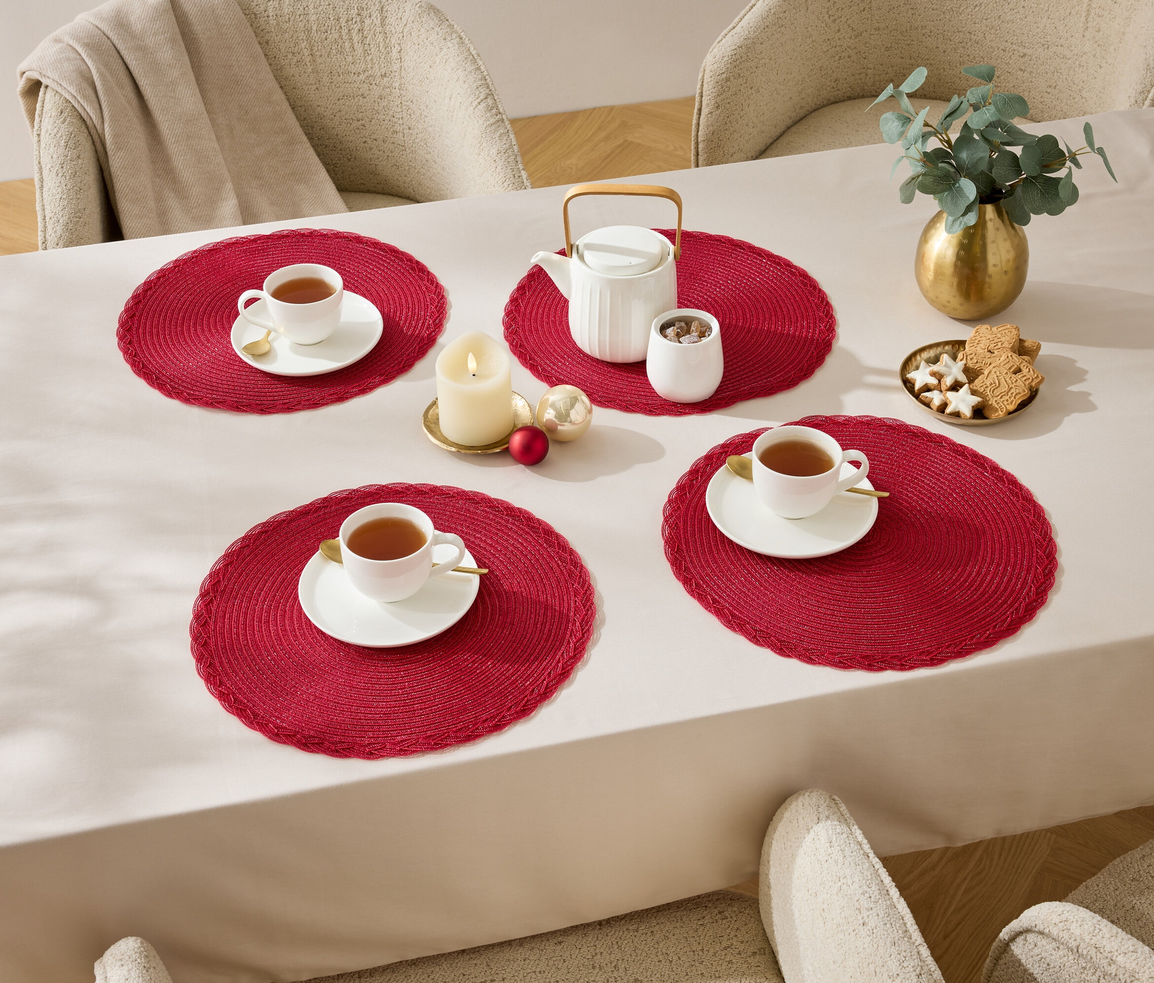 Vier Tassen auf roten Platzsets auf einem Tisch mit weißer Tischdecke.