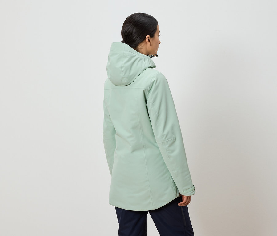 Rückansicht einer Frau in einer mintgrünen Kapuzenjacke und dunkelblauen Hosen.