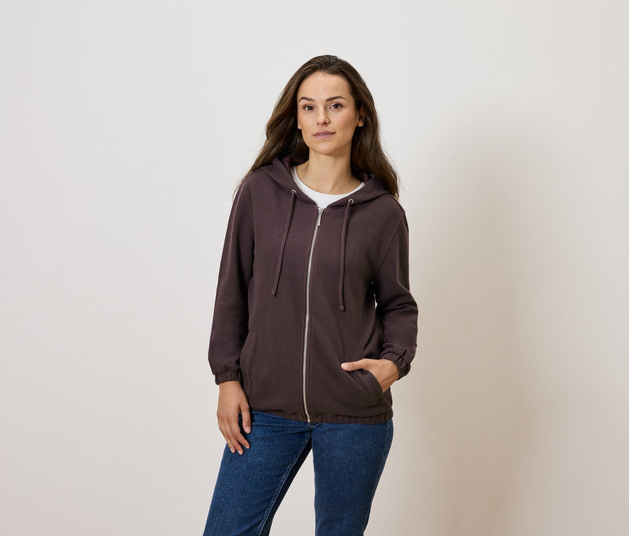 Frau posiert in braunem Reißverschluss-Hoodie und blauen Jeans.