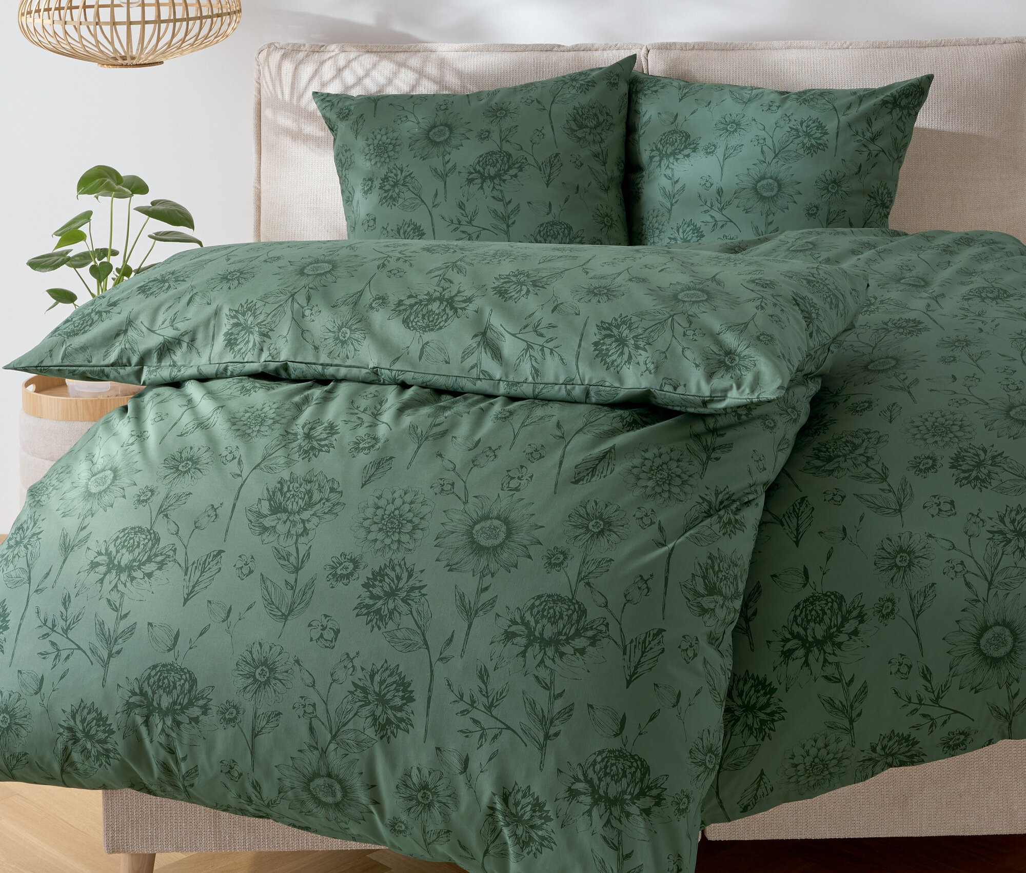 Grüne Bettwäsche mit Blumenmuster auf einem Bett.