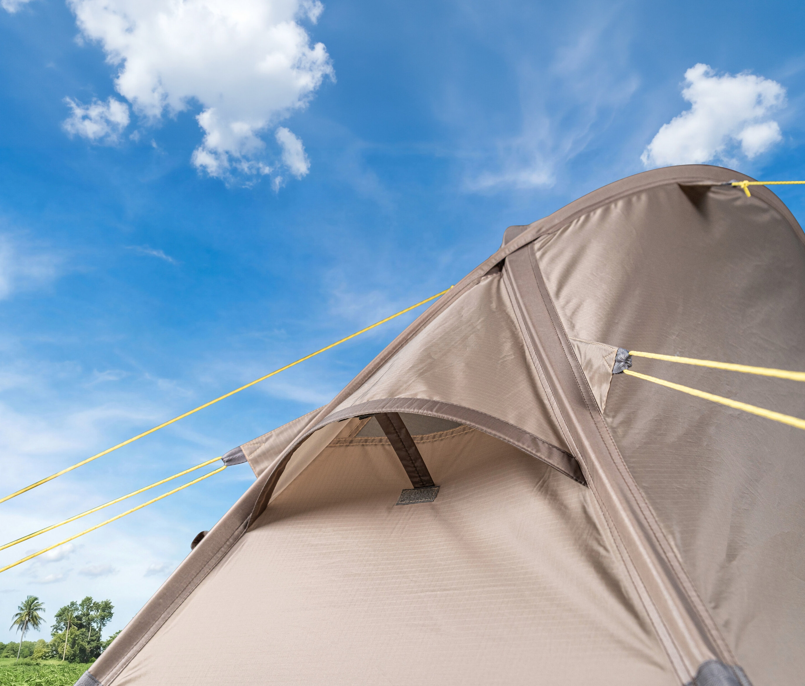 Nahaufnahme des Tambu 1-Personen-Trekkingzelts »ANDITO« mit gelben Spannseilen vor blauem Himmel.