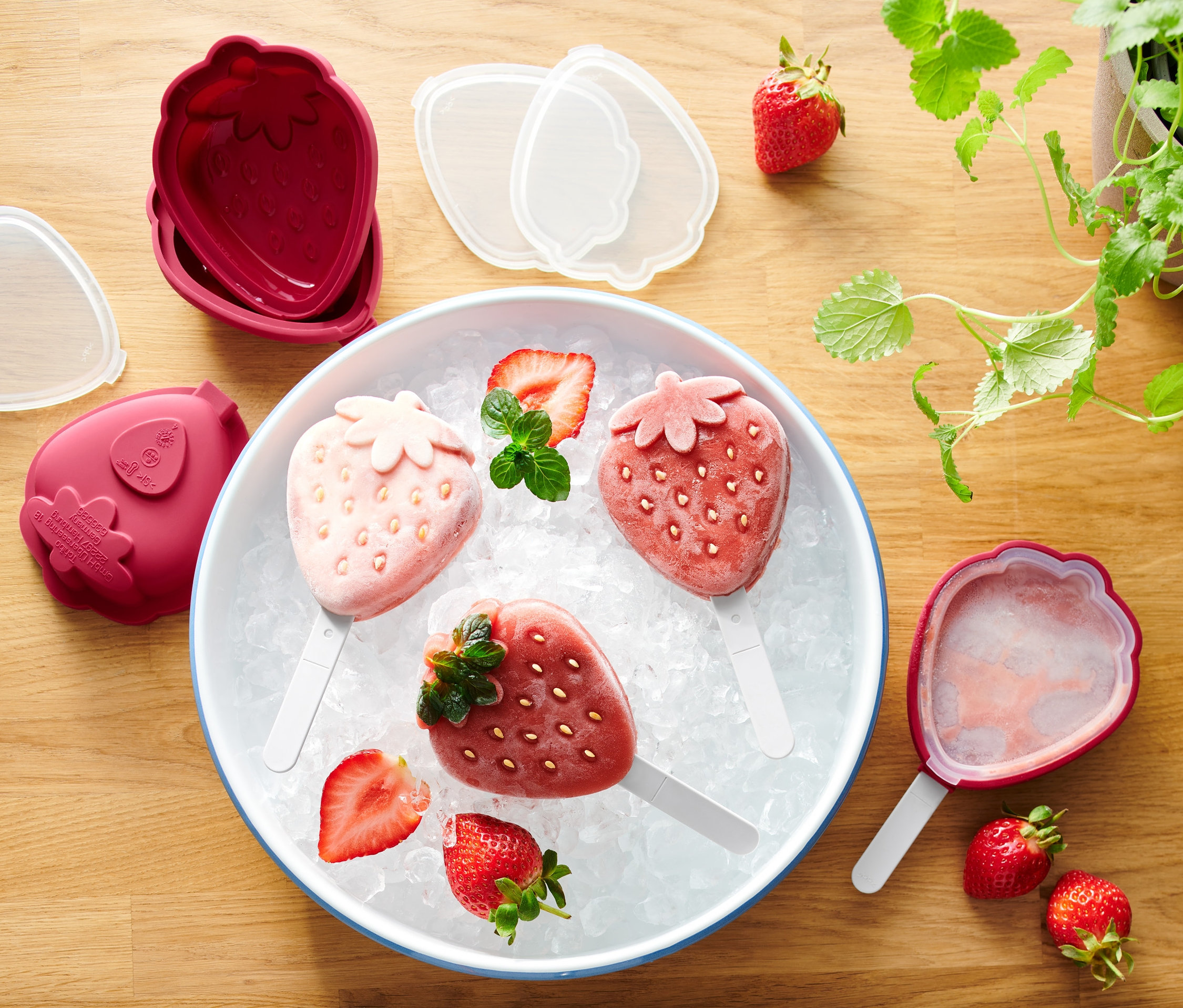 Drei Erdbeer-Eis am Stiel auf Eis in einer Schüssel neben 4 Eisformen.