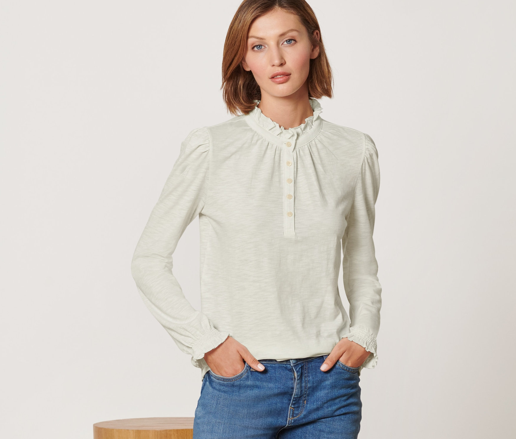 Frau posiert in einem Langarmshirt mit Rüschen und Jeans.