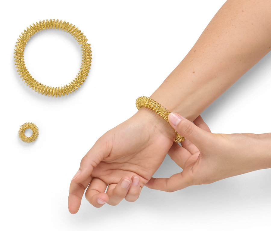 Frau zieht goldenen Akupressurring aus dem Akupressur-Set auf ihr Handgelenk. Zwei weitere Ringe liegen daneben.