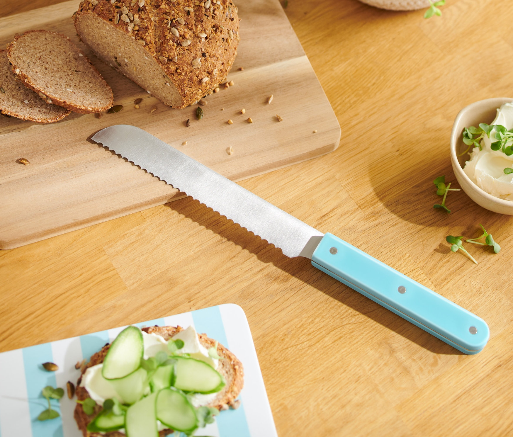 Brot und zwei Scheiben auf einem Holzbrett mit einem Küchenmesser mit blauem Griff.