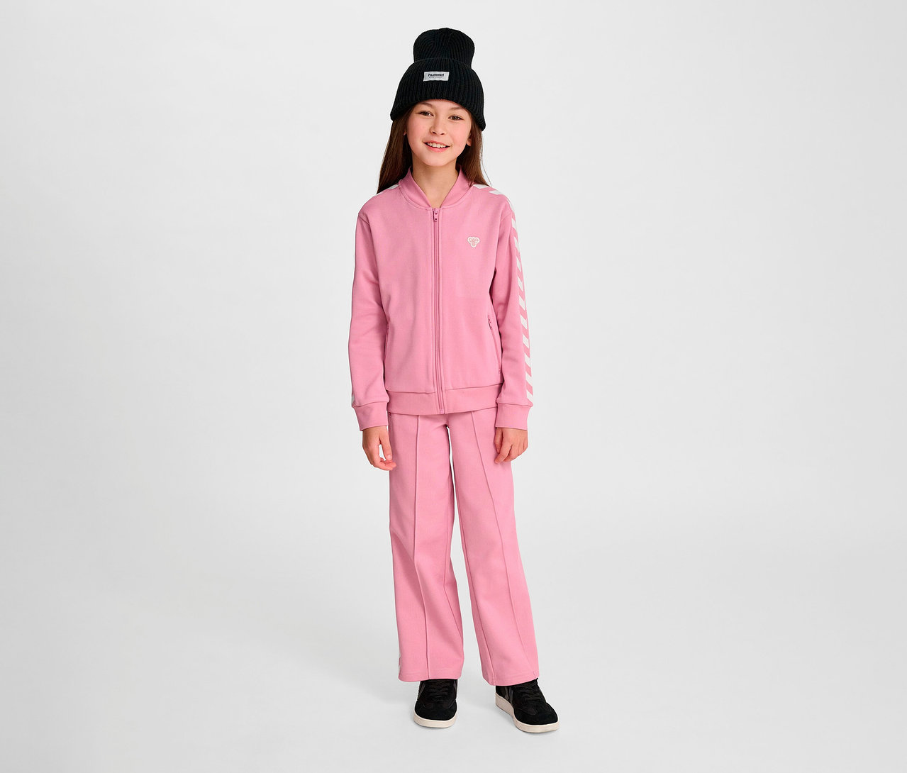 Mädchen trägt rosa Hummel HMLJR Archive Reg Poly Zip Jacket mit schwarzer Mütze.