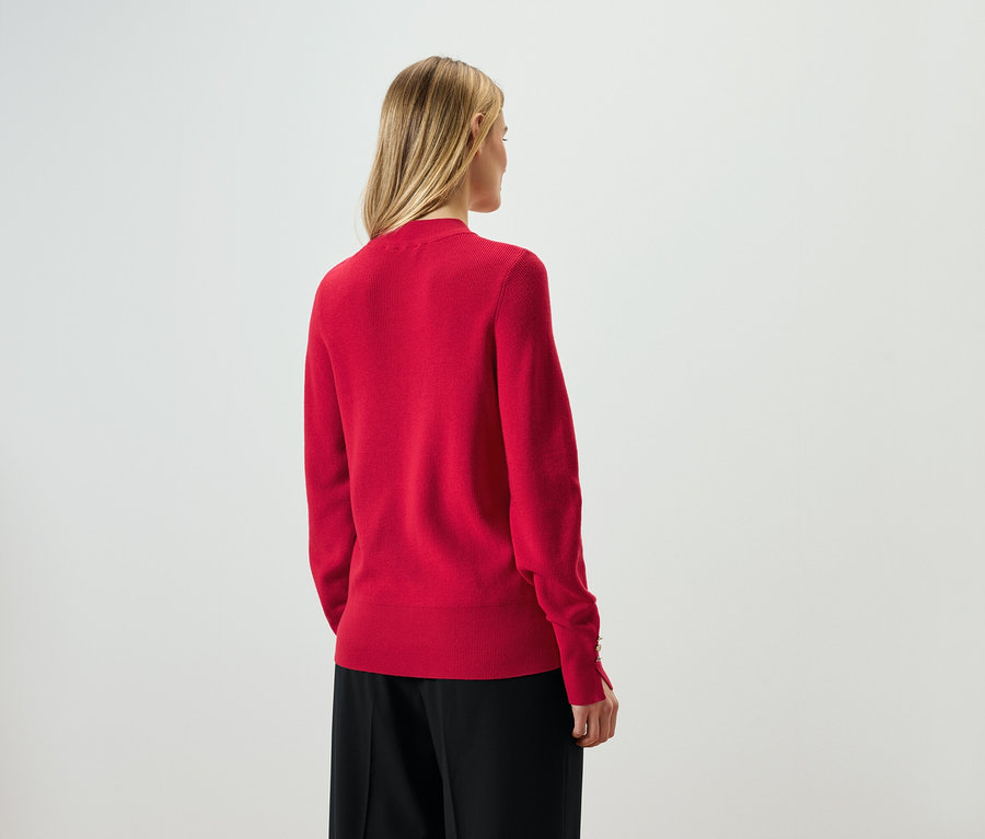 Von hinten ist eine Frau mit blonden Haaren in einem roten Pullover und einer schwarzen Hose zu sehen.