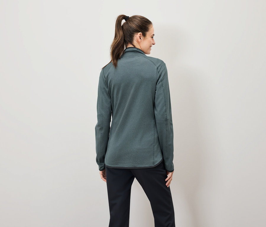 Von hinten sieht man eine Frau mit braunen, zu einem Pferdeschwanz zusammengebundenen Haaren, die eine grüne Sweatshirtjacke mit Reißverschluss und eine schwarze Hose trägt.