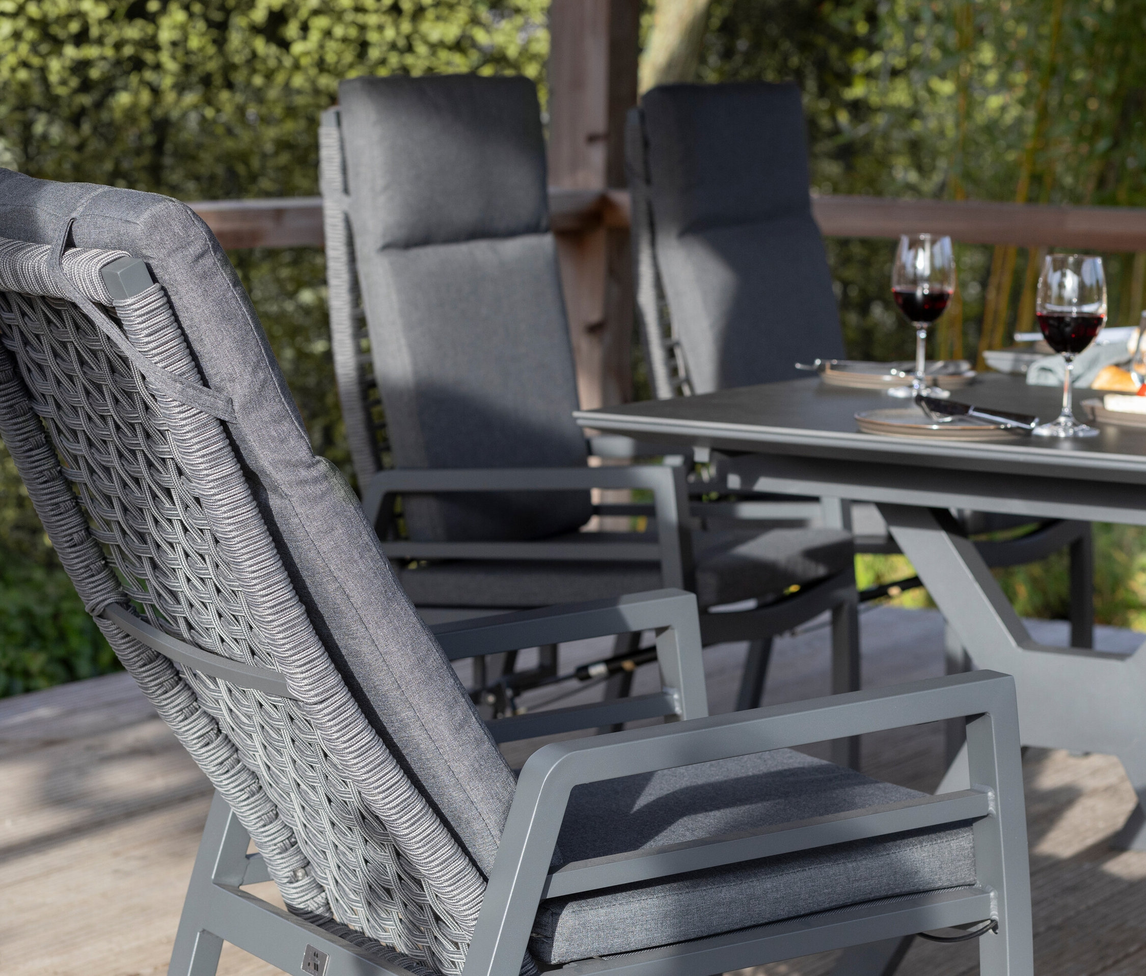 Detailansicht von grauen deVries Gartenstühlen mit Seilgeflecht und Polstern, Tisch mit Erfrischungen und Weingläsern auf einer Terrasse.