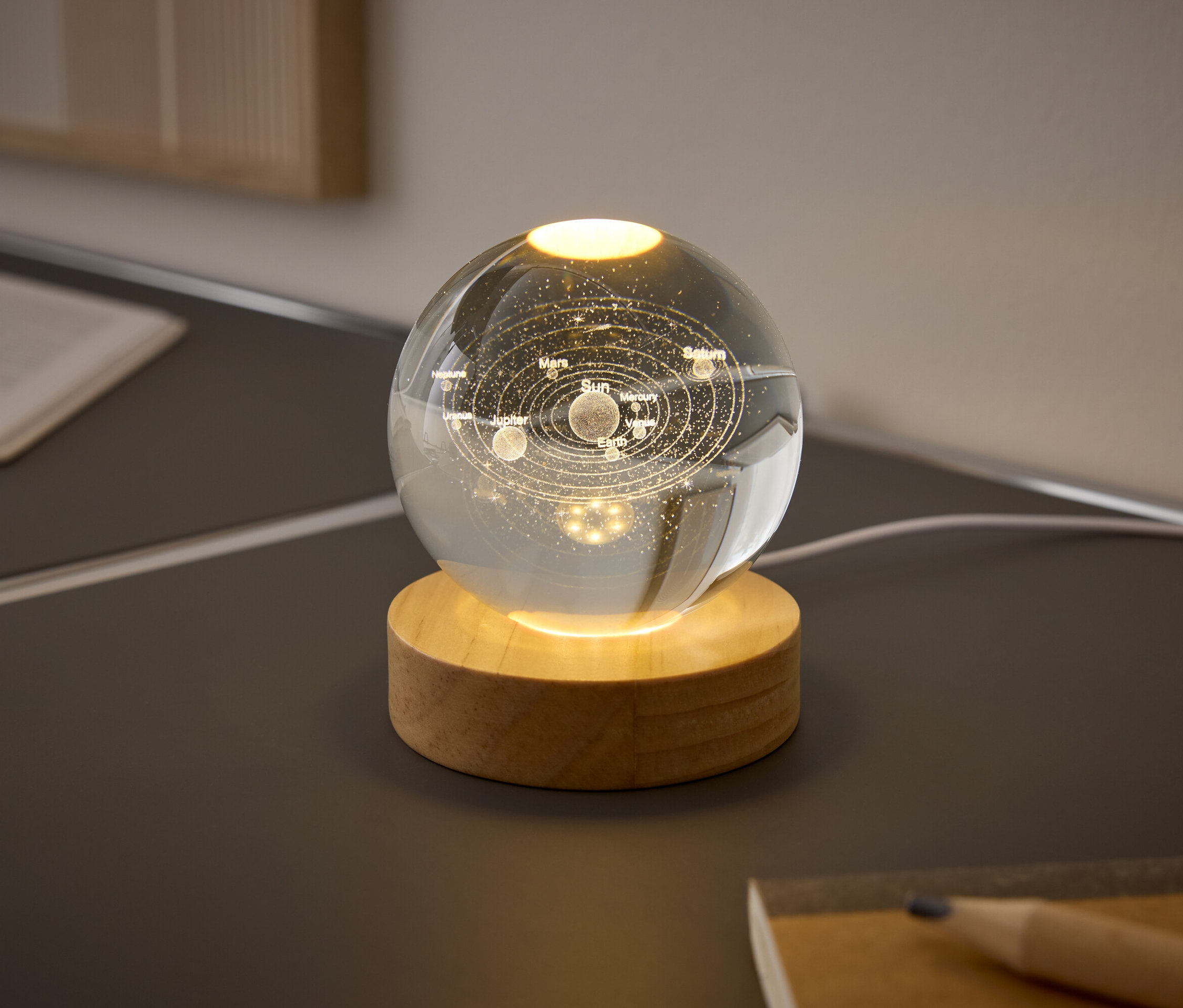 Eine Glaskugel mit den Planeten des Sonnensystems auf einem Holzsockel leuchtet auf einem Tisch.