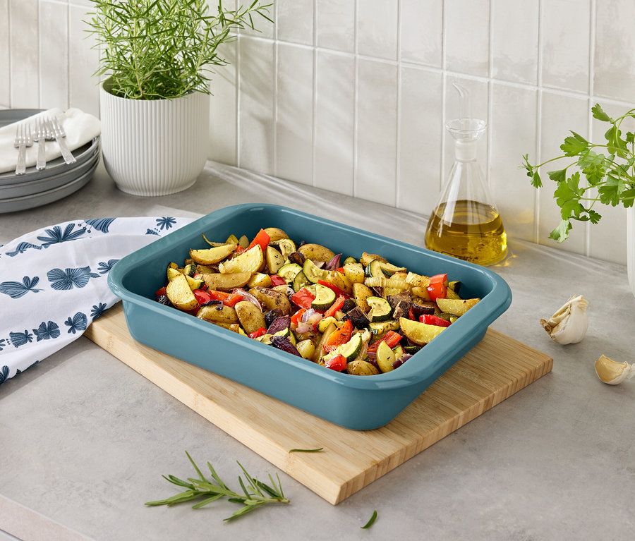 Gebackene Kartoffeln mit Gemüse in einer blauen Auflaufform auf einem Holzbrett.