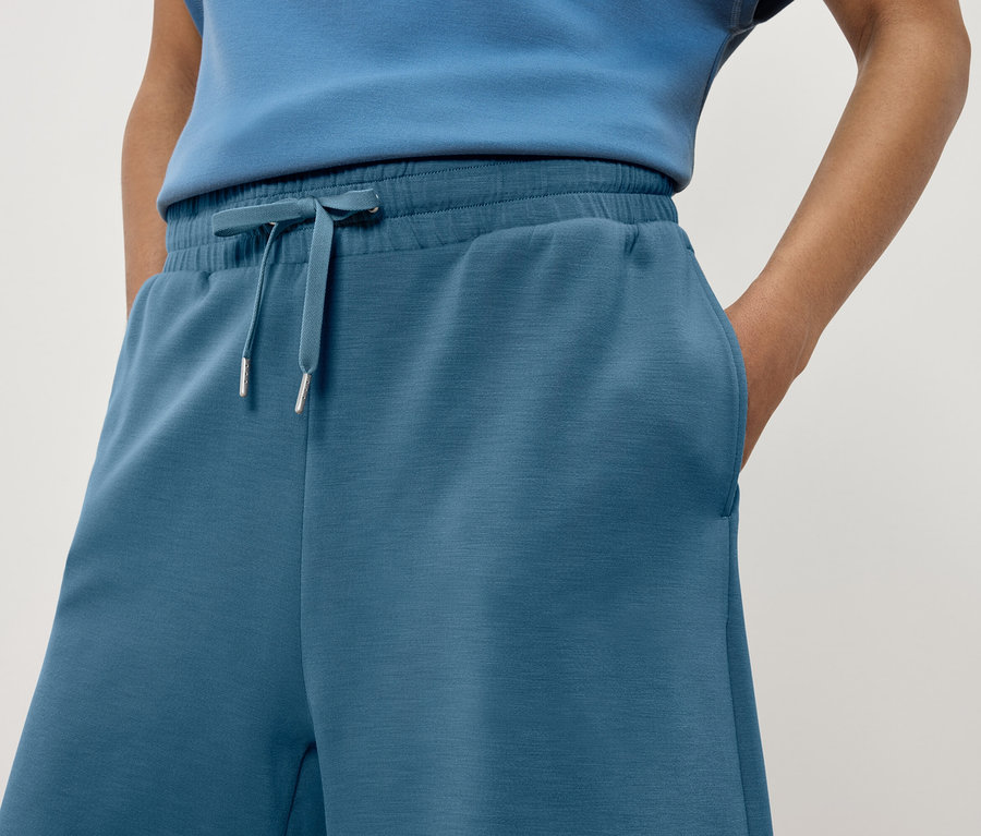 Detailaufnahme einer Frau, die blaue Trainingshose mit einer Hand in der Tasche trägt.