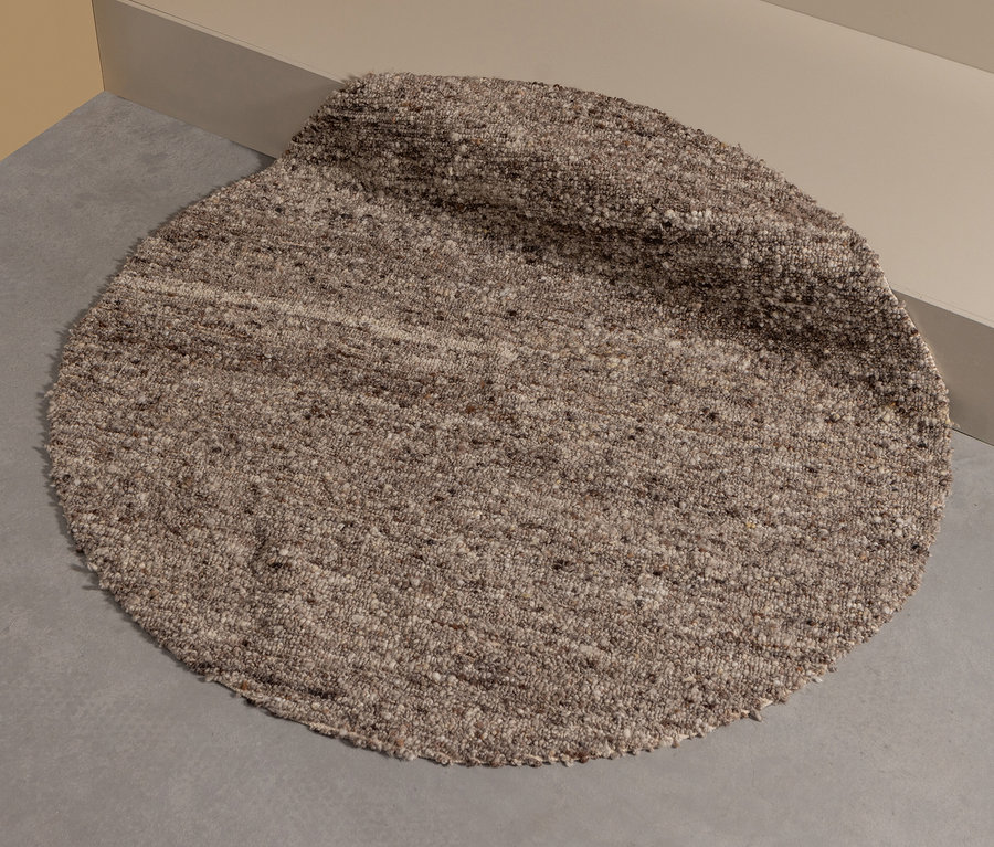 Ein beiger, runder Woood Teppich »Efia«, Ø 200 cm, liegt auf dem Boden neben einer Treppe.