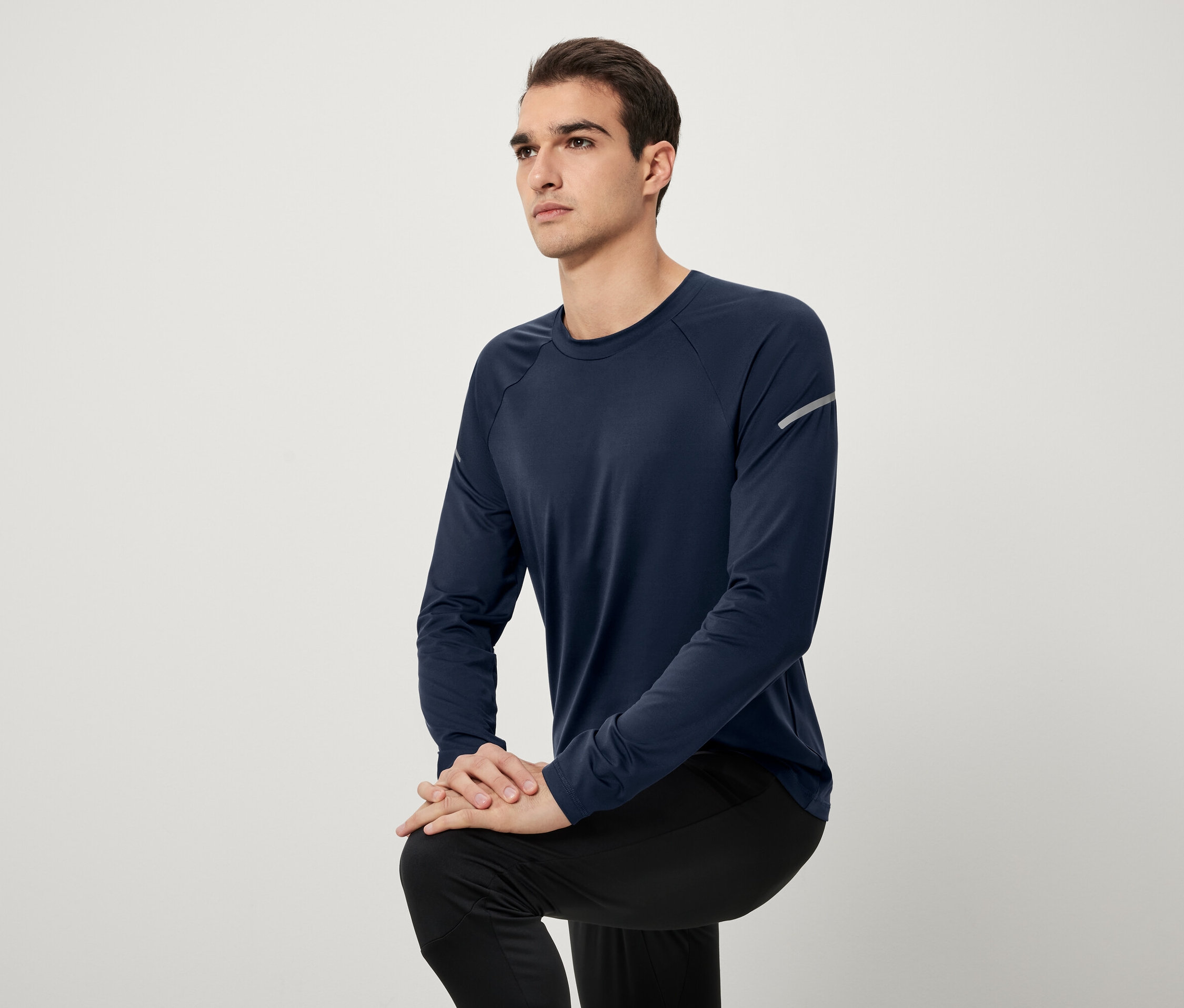 Mann posiert in dunkelblauem Langarmshirt und schwarzer Hose.