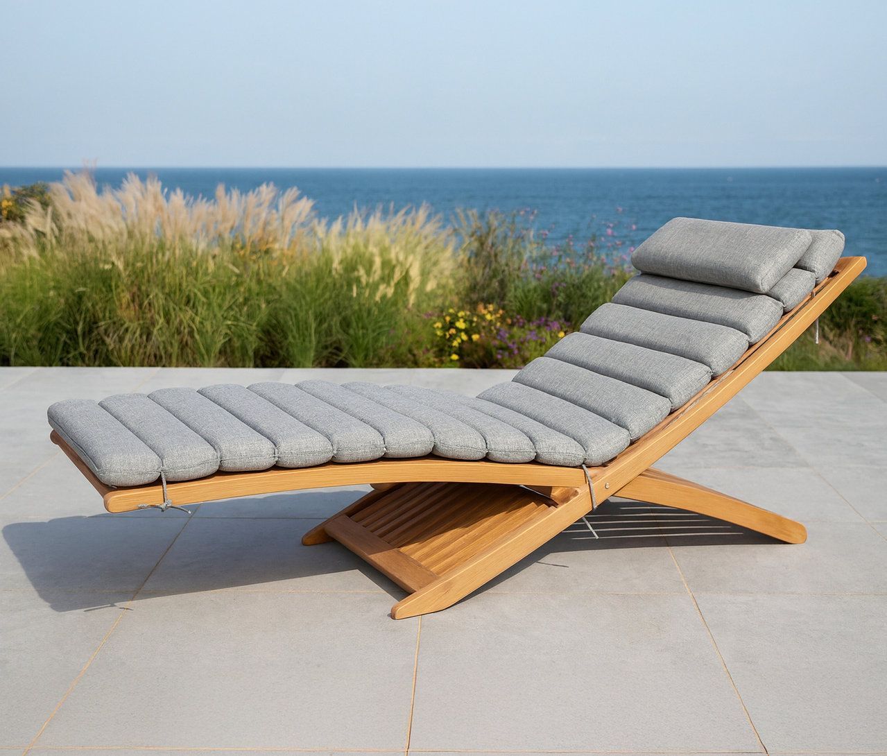 Eine Leco Sonnenliege mit grauem Polster steht auf einer Terrasse mit Meerblick.