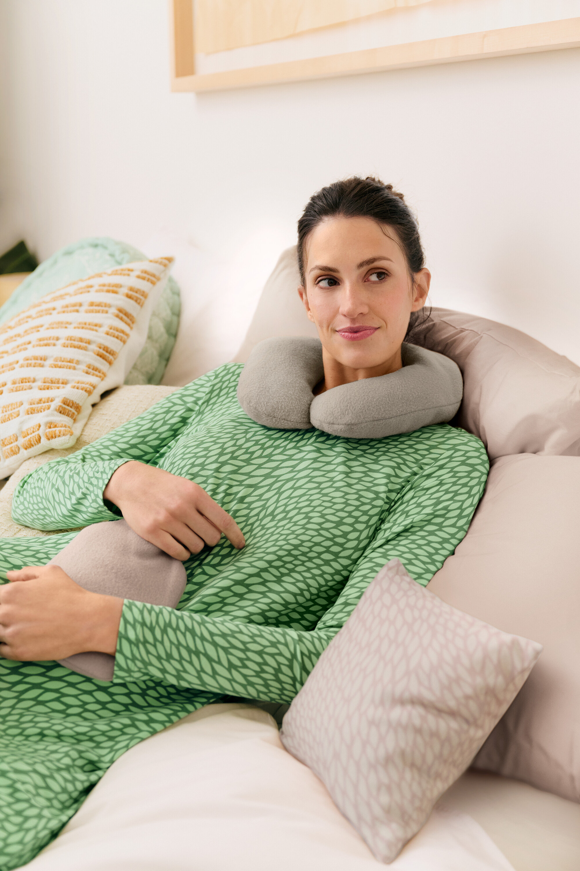 Frau liegt mit grauer Nackenrolle und Wärmflasche im Bett und trägt ein grünes Nachthemd.