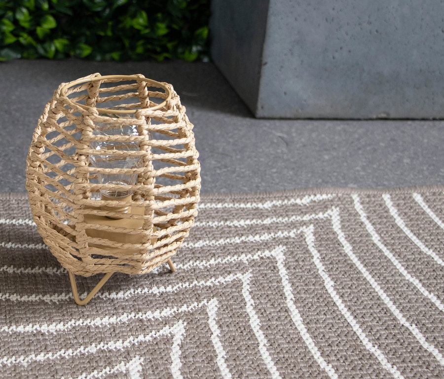 Dekorative Lampe im Rattankorbdesign steht auf einem Teppich mit Zickzackmuster.