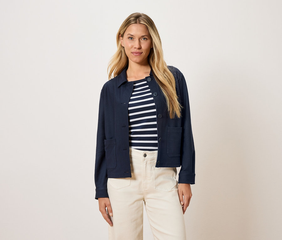 Frau trägt eine marineblaue Jacke über einem gestreiften Oberteil und cremefarbene Hosen.